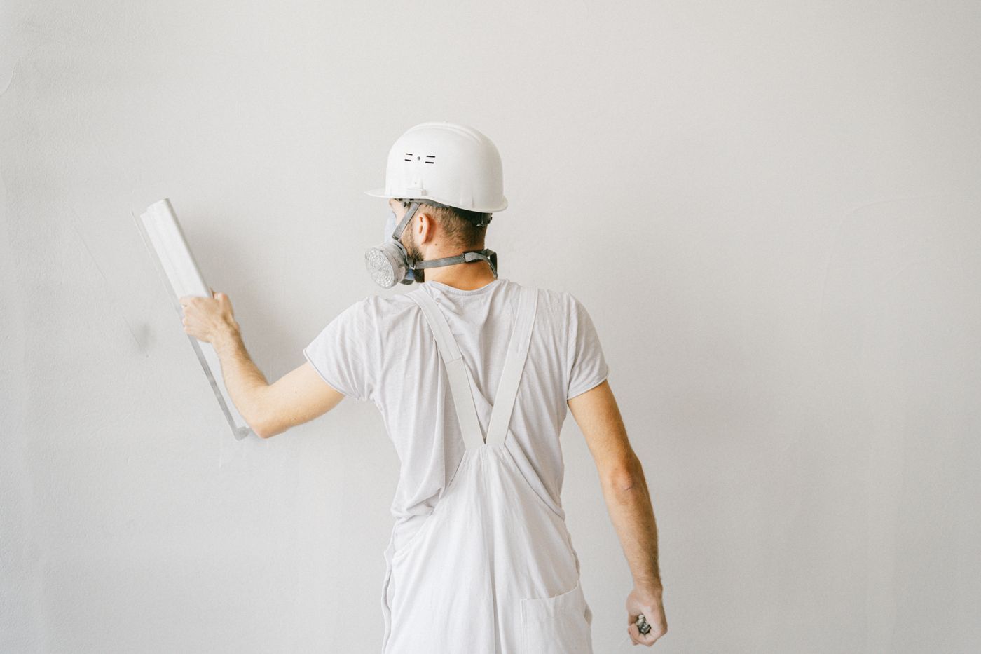 Man in witte overall werkt een witte wand af met een pleisterspaan